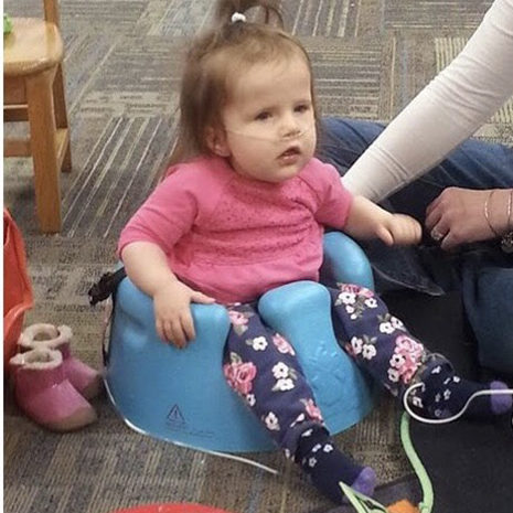 Baby with disabilities sitting in assistive technology chair.