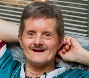 Older man with Down Syndrome sitting on couch enjoying smart home technology.