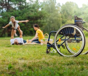 Child with a disability playing airplane with her parents next to wheelchair.